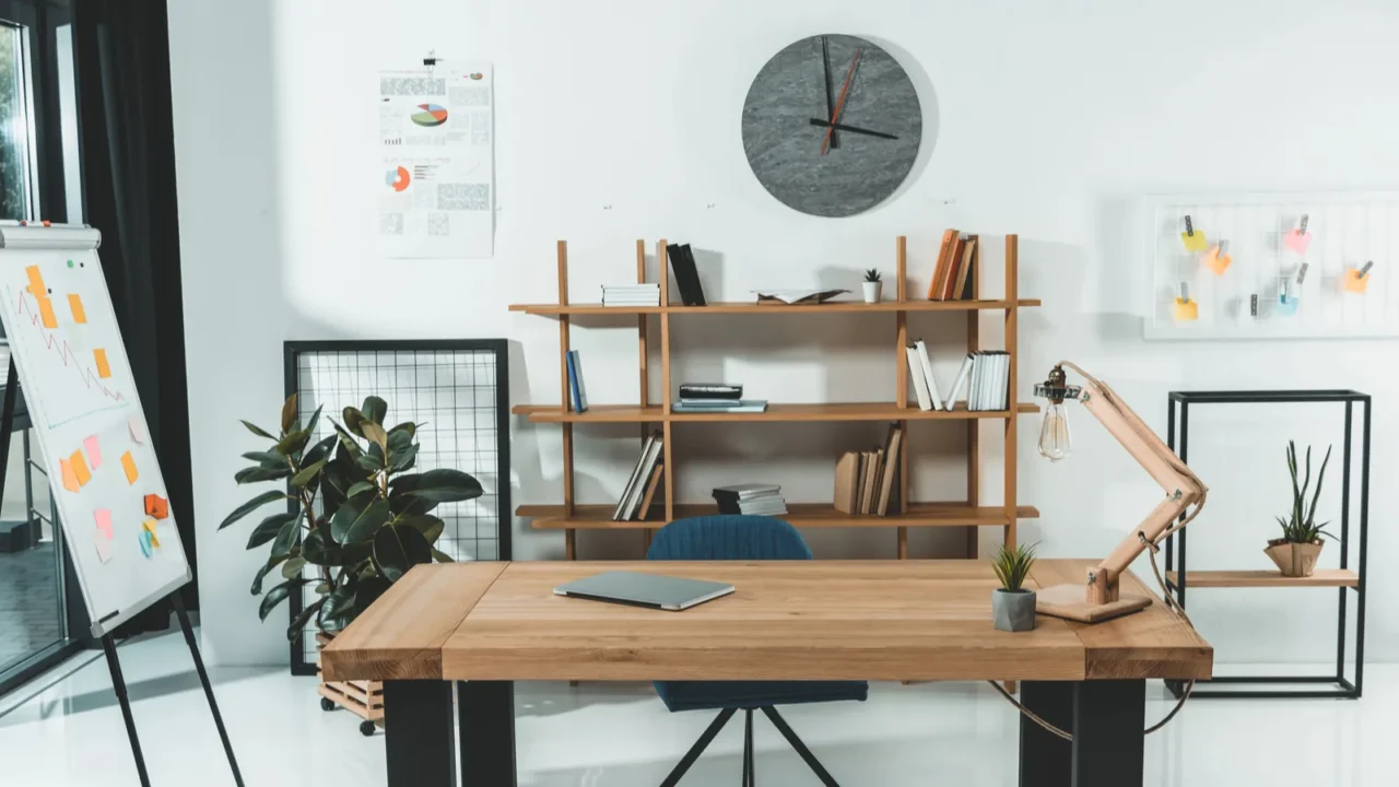 A home office interior with a wooden desk, bookshelf, whiteboard, and gray clock on the wall.