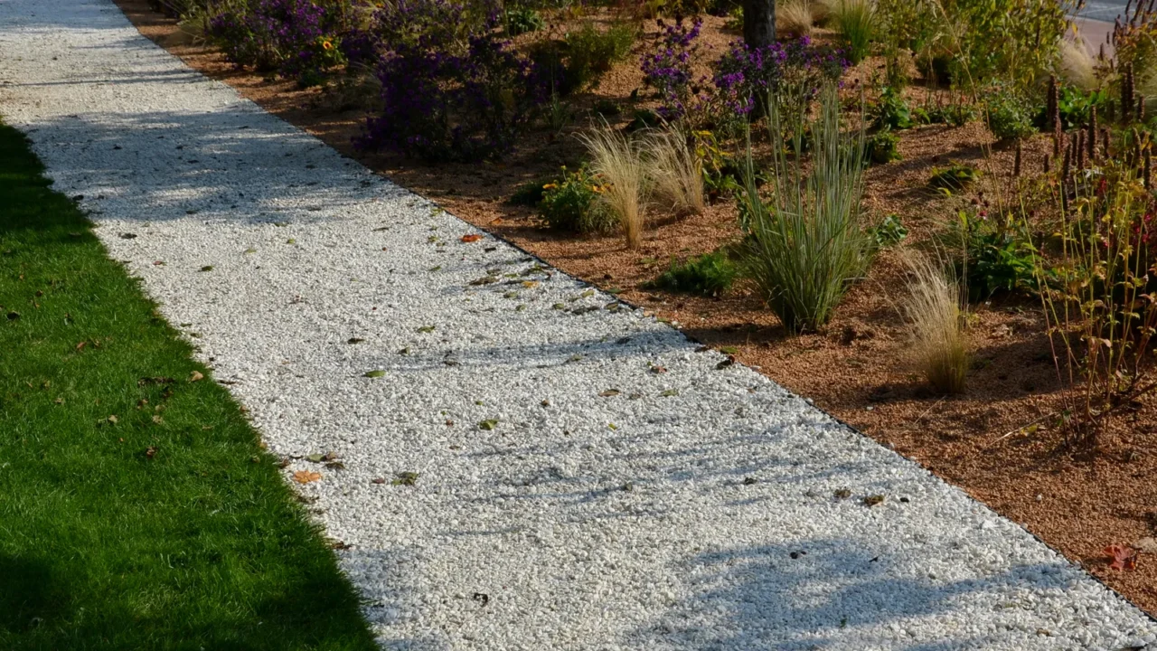 A garden with pea gravel path surrounded by plants and grasses.