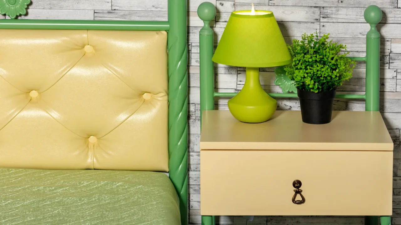 A nightstand and metal frame bed with pastel green painted frame and pastel yellow drawer and headboard.