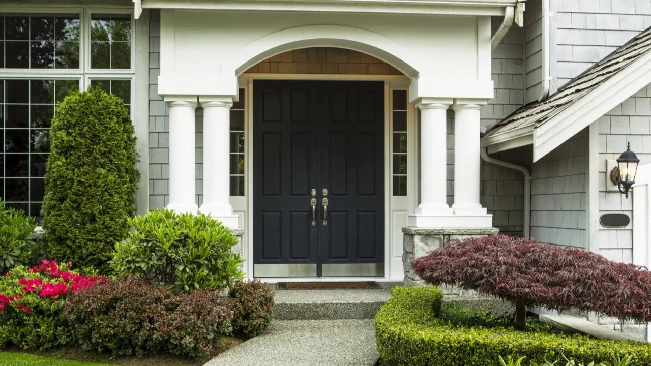 A charming entryway with a dark front door, columns, and well-kept landscaping.