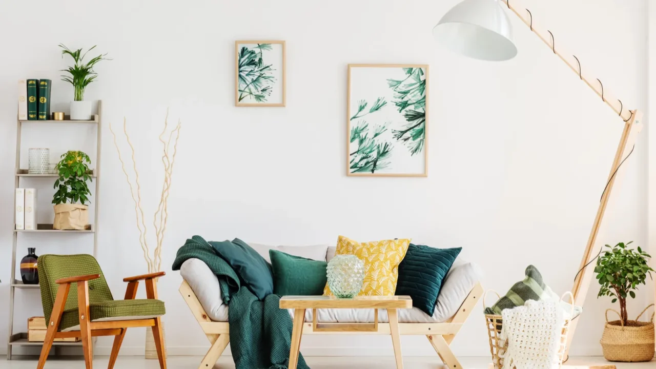 A living room interior with wooden sofa and coffee table, floor lamp, armchair, shelf with decor accents, and framed artwork on the wall.