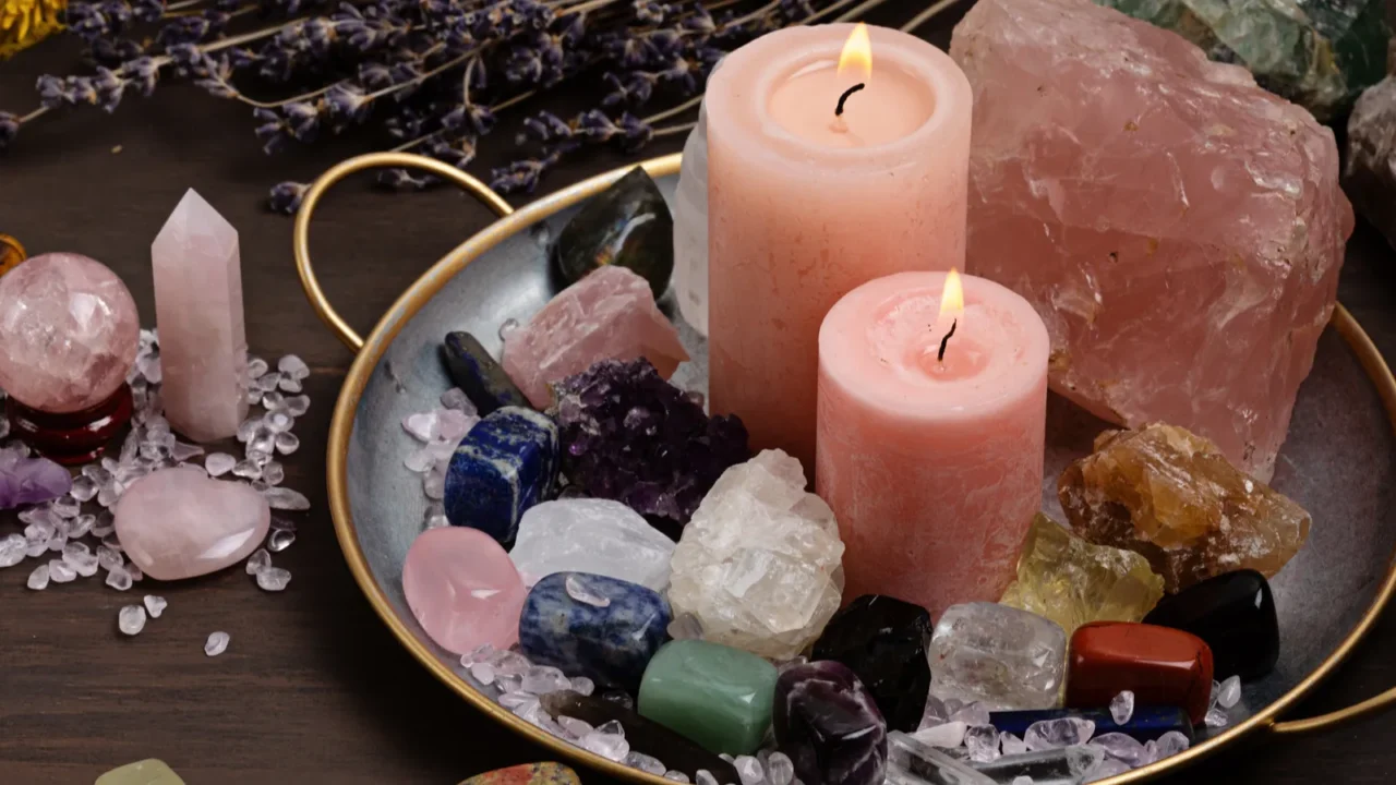 A decorative tray with various crystals and two pink candles on a dark surface.