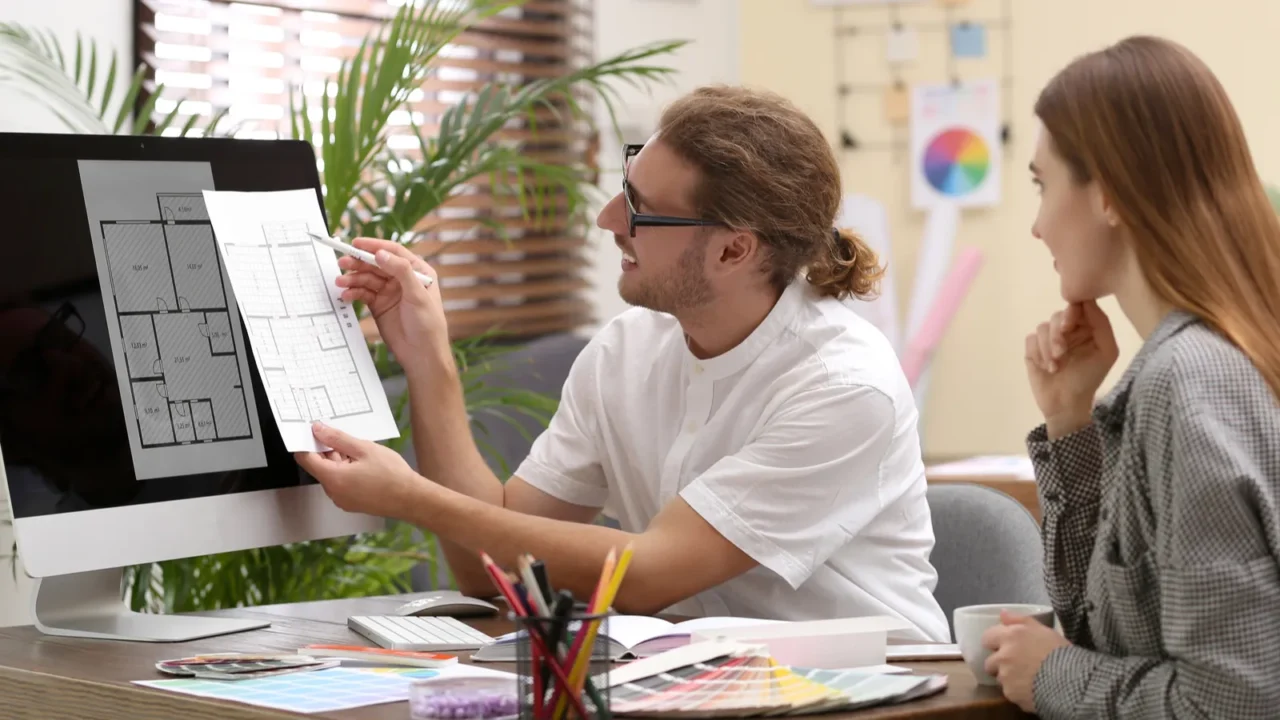 An interior designer consulting with a young woman in office, showing her layout design.
