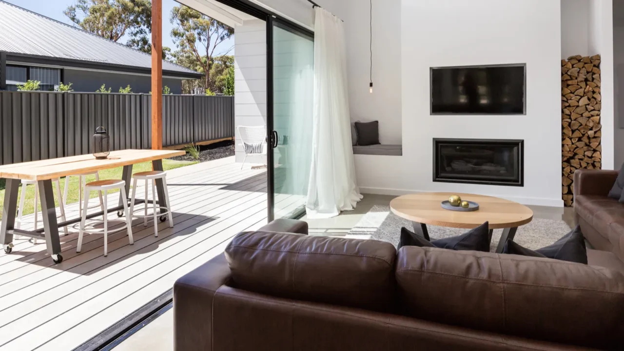 An outdoor patio with a wooden dining table, white chairs, and a view of the garden, bathed in natural sunlight.