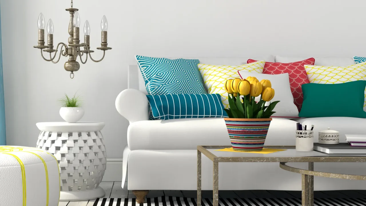 A stylish living room interior with a cozy white sofa with patterned throw pillows, rug, coffee table with painted plant pot, and a chandelier hanging from the ceiling.