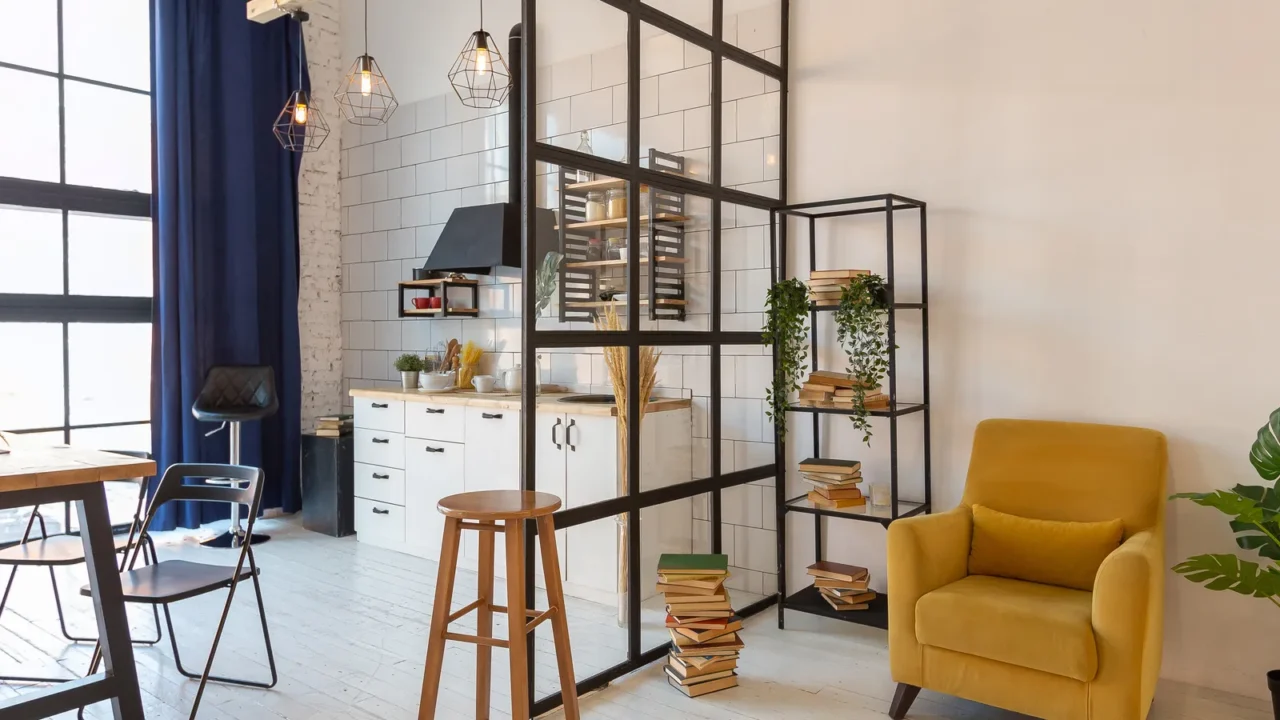 A modern kitchen and living space separated by a black glass partition.