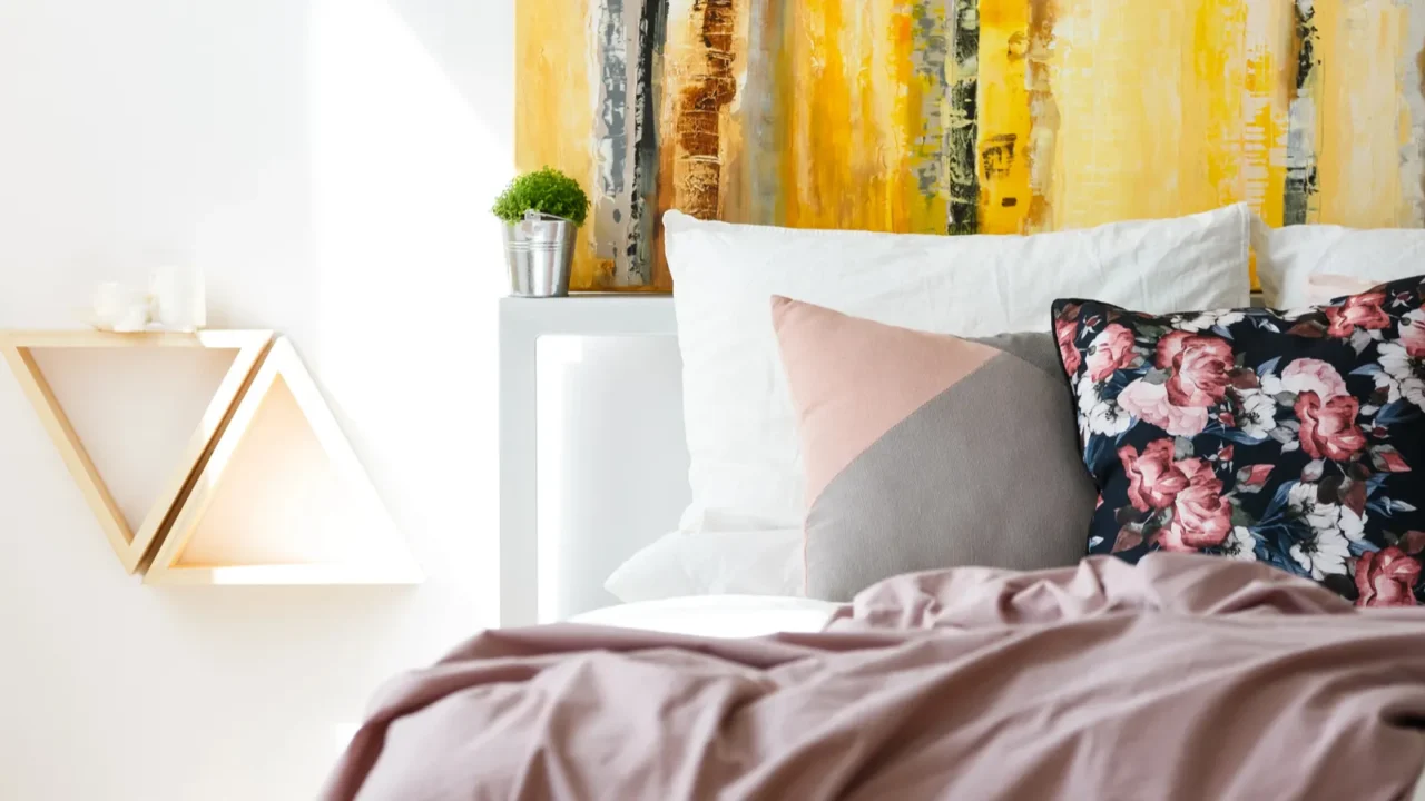 A bed with pastel pink bedding, floral and pastel cushions, and white pillows.