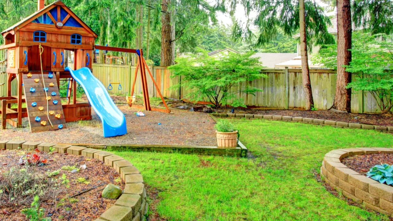 A colorful playground with a wooden treehouse, slide, and swing set amid green trees.