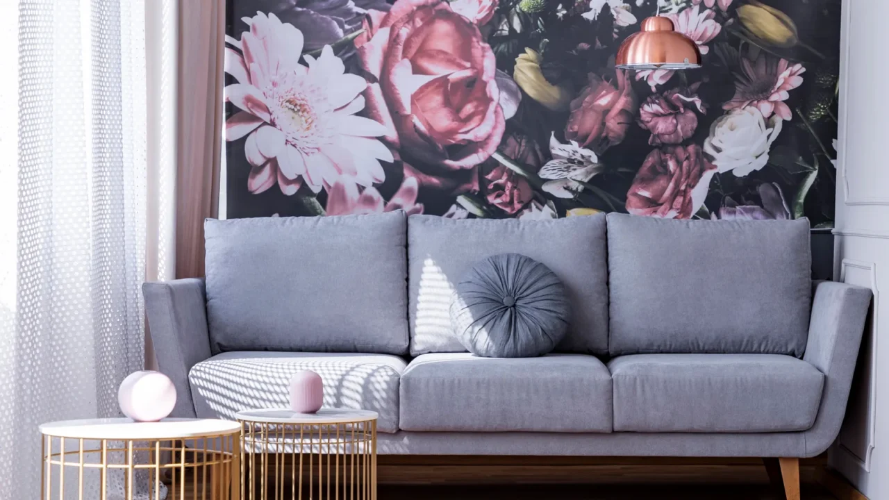 A bright living room interior with nesting coffee tables and gray sofa in front of a wall with floral wallpaper.