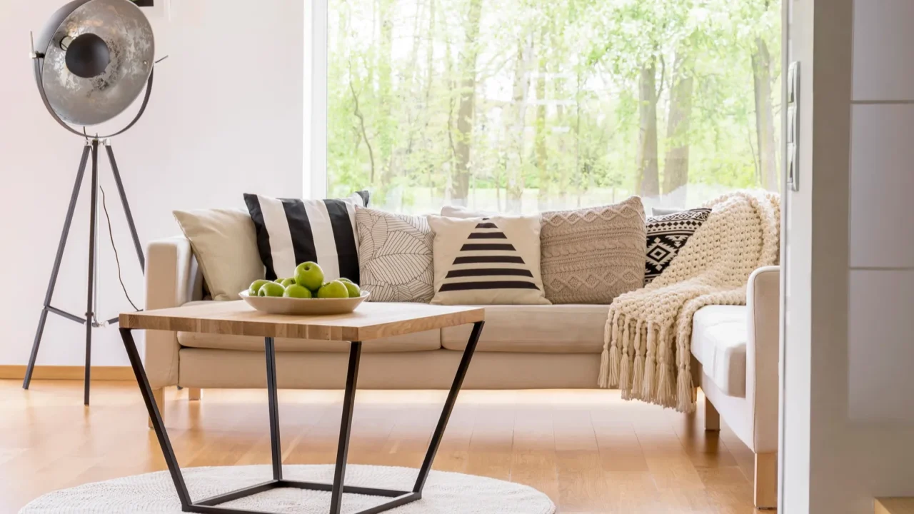 A comfortable linen sofa with throw pillows and throw blanket and a wooden coffee table with apples in a plate on it in a living room.