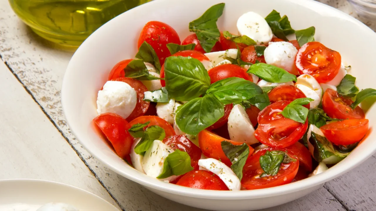 A fresh salad with cherry tomatoes and mozzarella balls topped with basil.