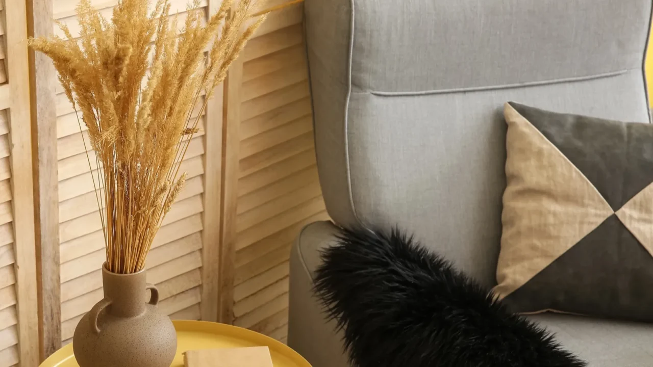 vase with wheat spikelets on table and armchair near folding