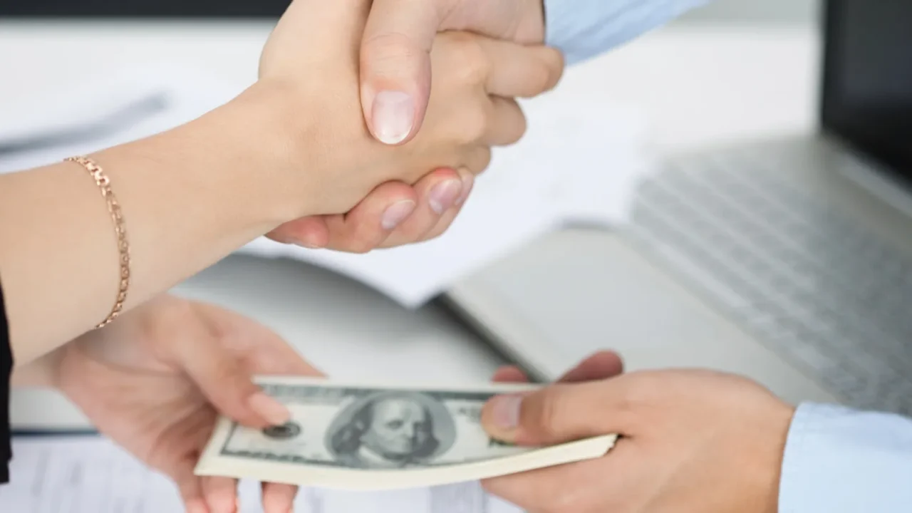 A handshake over a money exchange, likely in a business transaction.