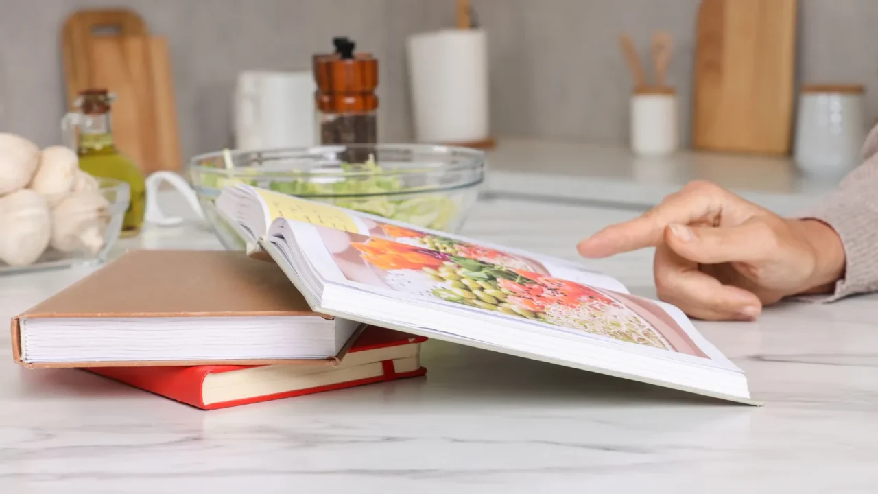 woman with recipe book at table in kitchen closeup