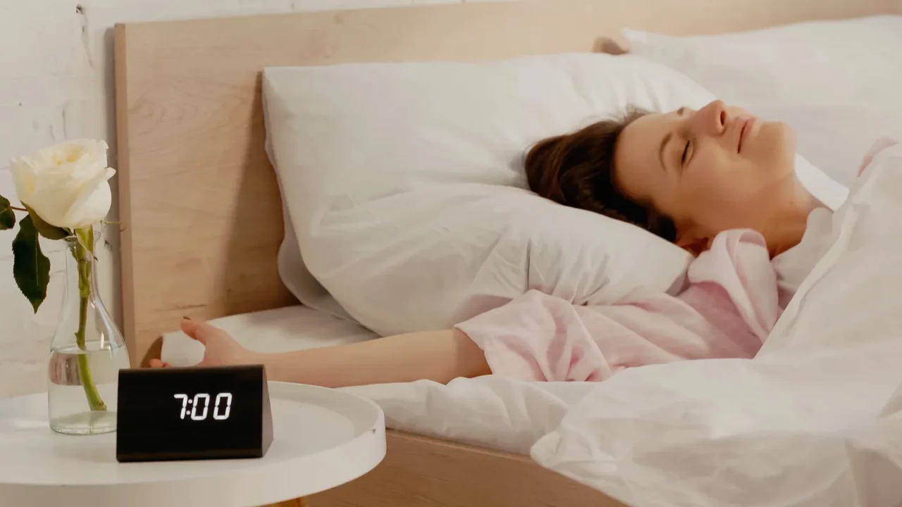 young brunette woman lying n bed near clock on bedside