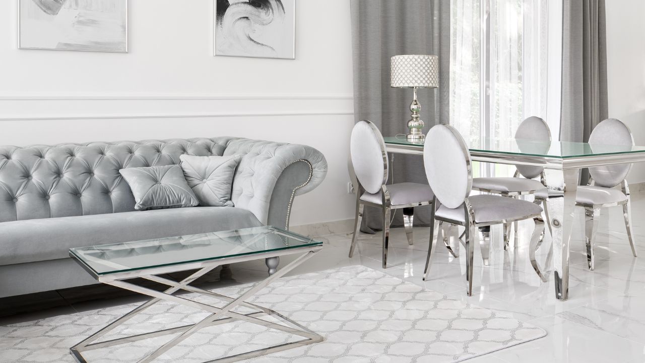 A white living room with a tufted sofa, glass coffee table, and light-colored curtains.