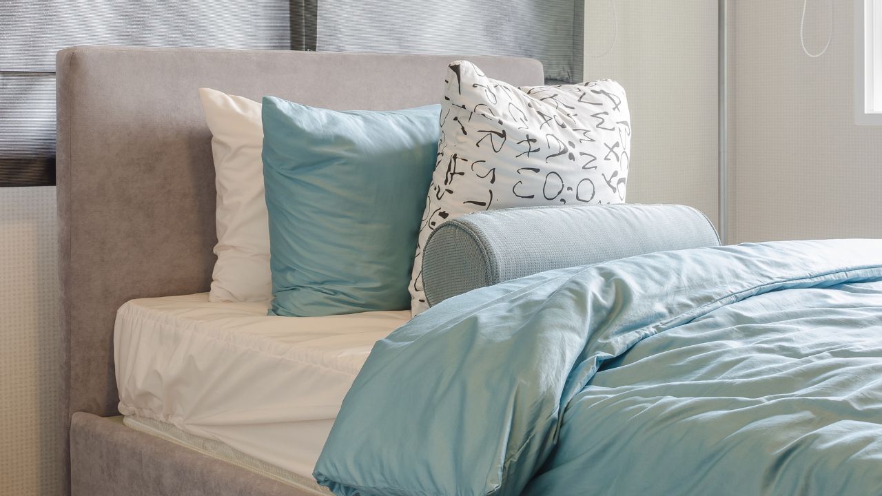 A bedroom with a bed that has white and light blue sheets, pillows, and a headboard.