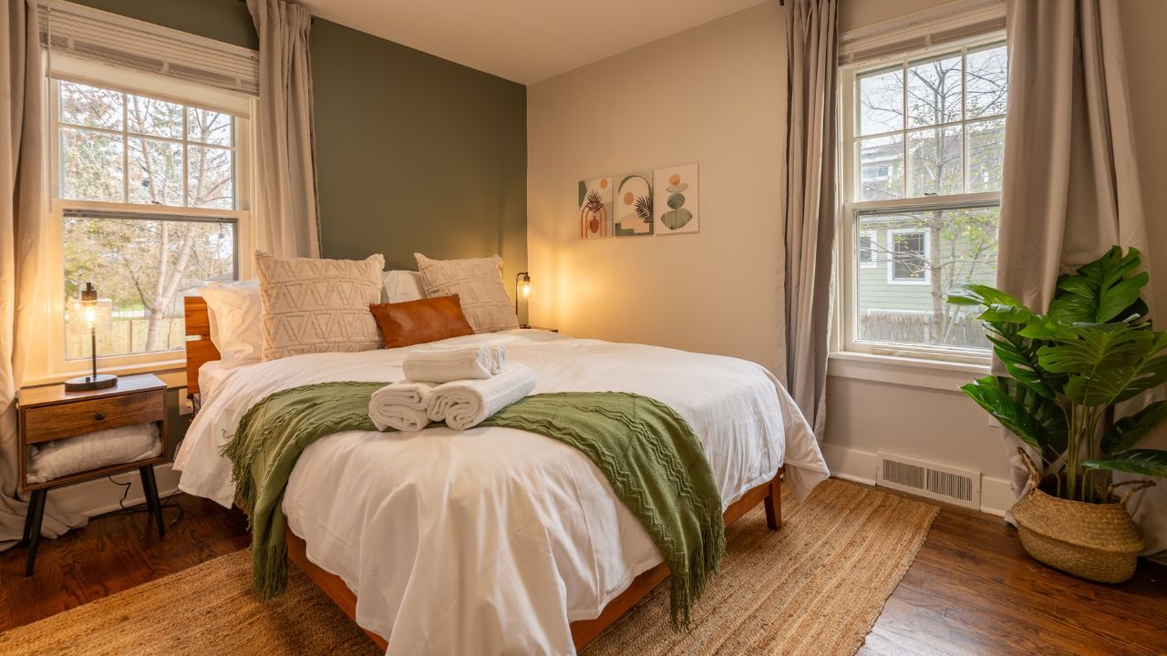 Bright bedroom with a bed, green blanket, and large windows.
