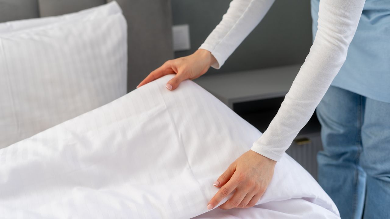 A person making a bed with white sheets and pillows.