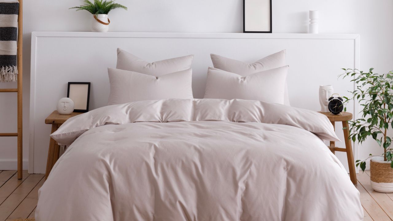 A neatly made bed with light pink bedding, pillows, and wooden side tables in a minimalist styled bedroom.