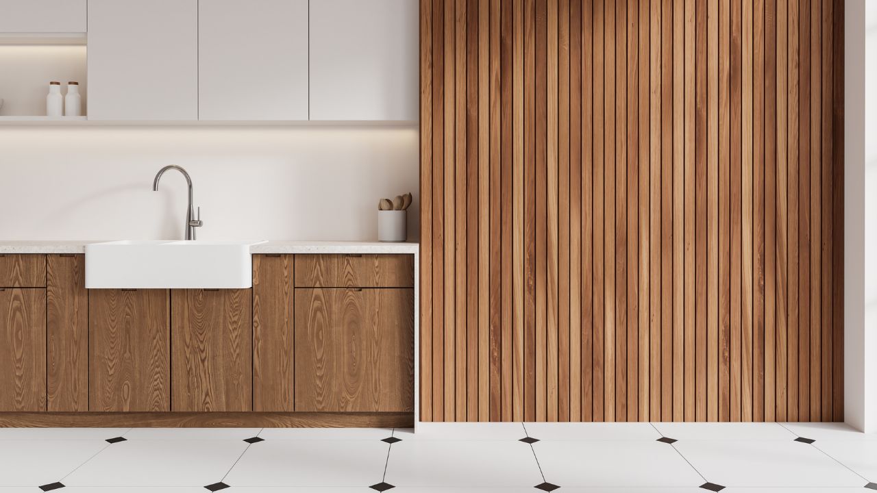 A modern kitchen with white cabinets, a white farmhouse sink, and wooden paneling on the wall.