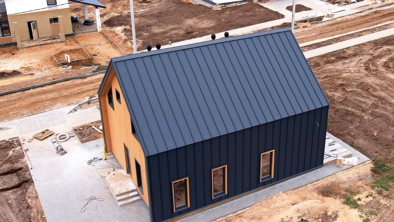A small modern house with black metal siding and wooden accents on a construction site.