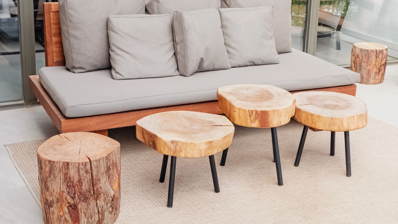 Lounge area with a grey cushioned sofa and natural wood stump tables on a rug.
