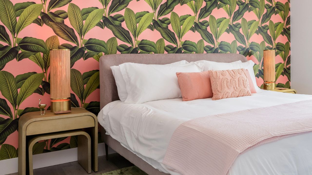 Bedroom with vibrant pink floral wallpaper, a large bed, and gold accent lamps.