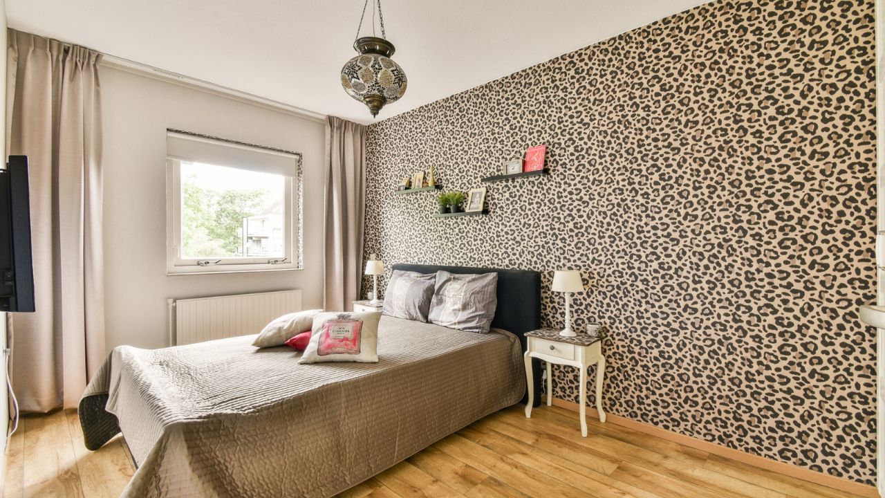Bedroom with beige bedding and a black headboard against a leopard print accent wall.