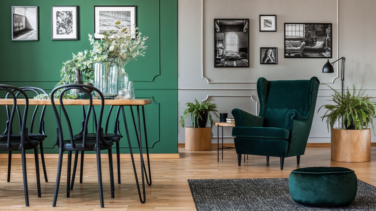 An elegant living room with black and white photos, green walls, and a green velvet armchair.