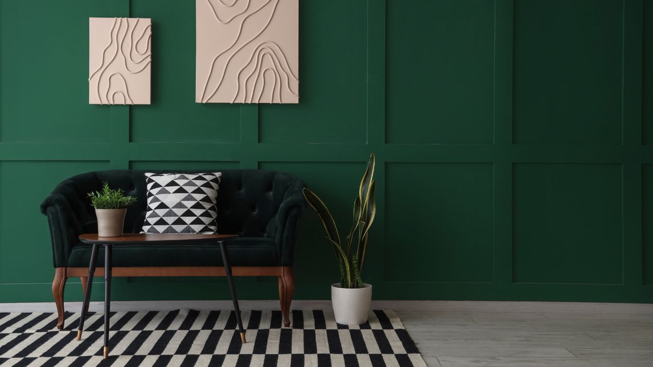 A cozy living room corner with a black velvet sofa, a small wooden table, and modern wall art on a green wall.