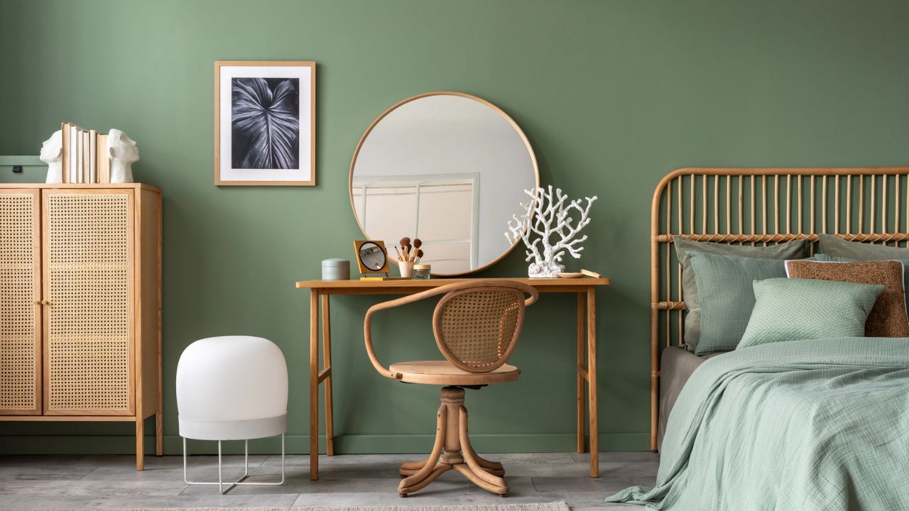 A stylish bedroom with green walls, a wooden dresser, and decorative wall art.