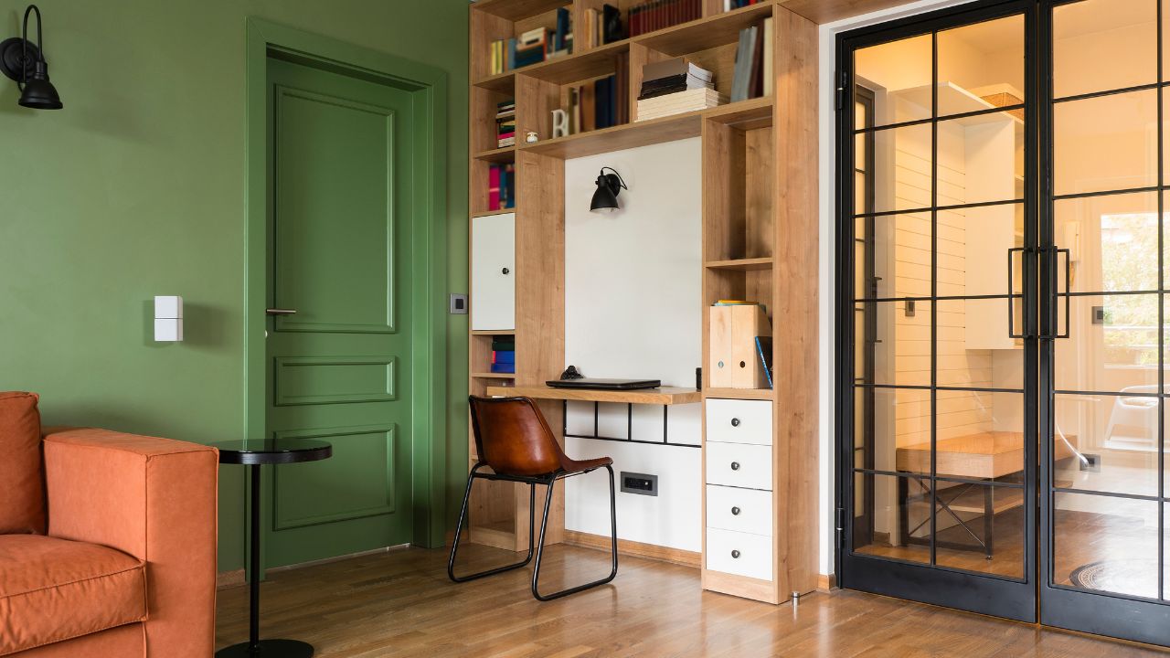 A cozy home office with green walls, a wooden desk, and bookshelves.