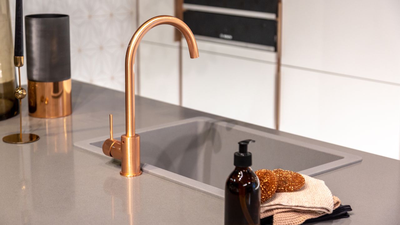 Kitchen sink with copper faucet and hand towel.