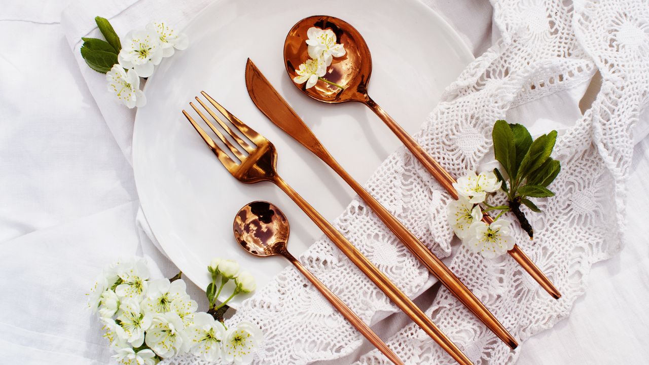 Stylish dining area with copper-colored cutlery, flowers, and lace fabric.