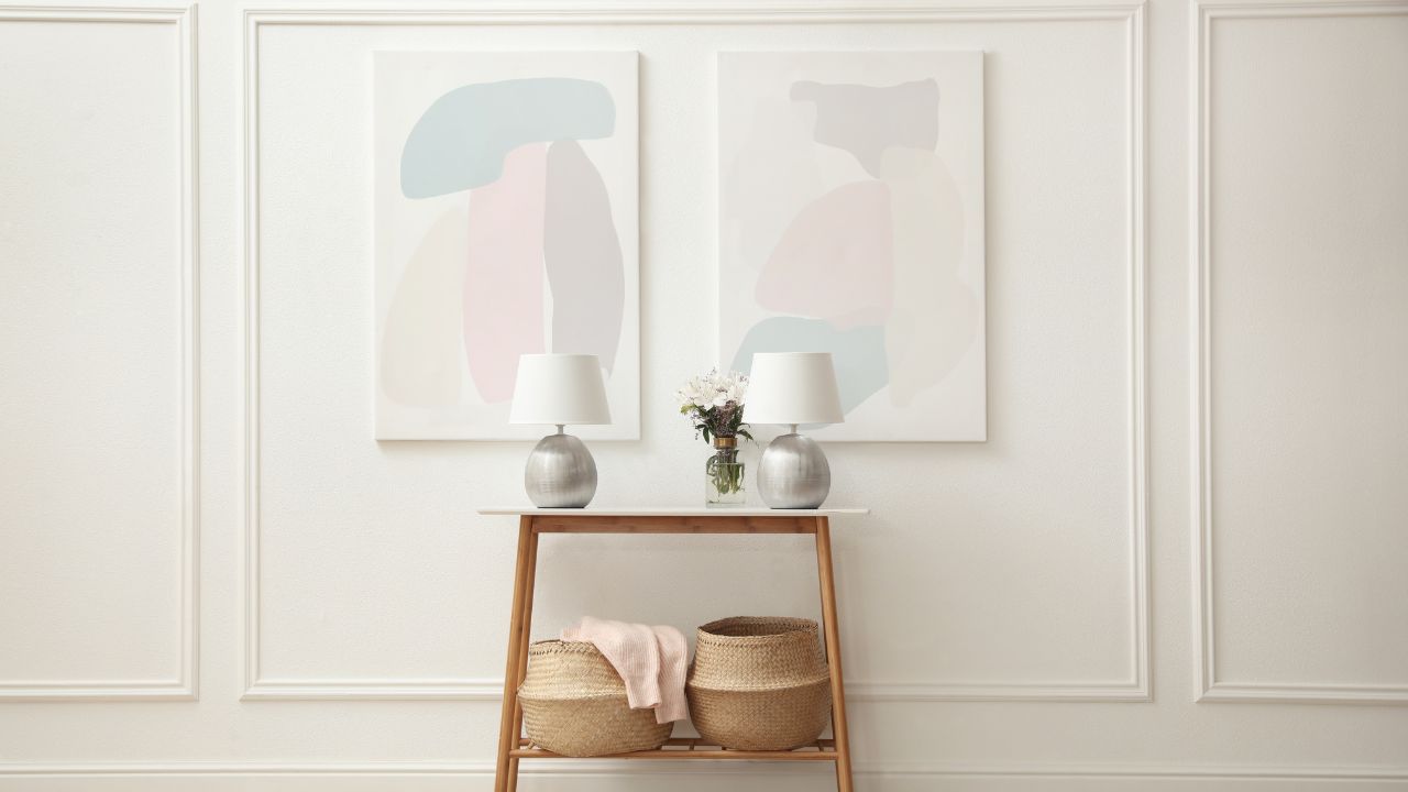 Minimalist hallway or entryway with abstract artwork, white walls, and a wooden console table decorated with lamps and baskets.