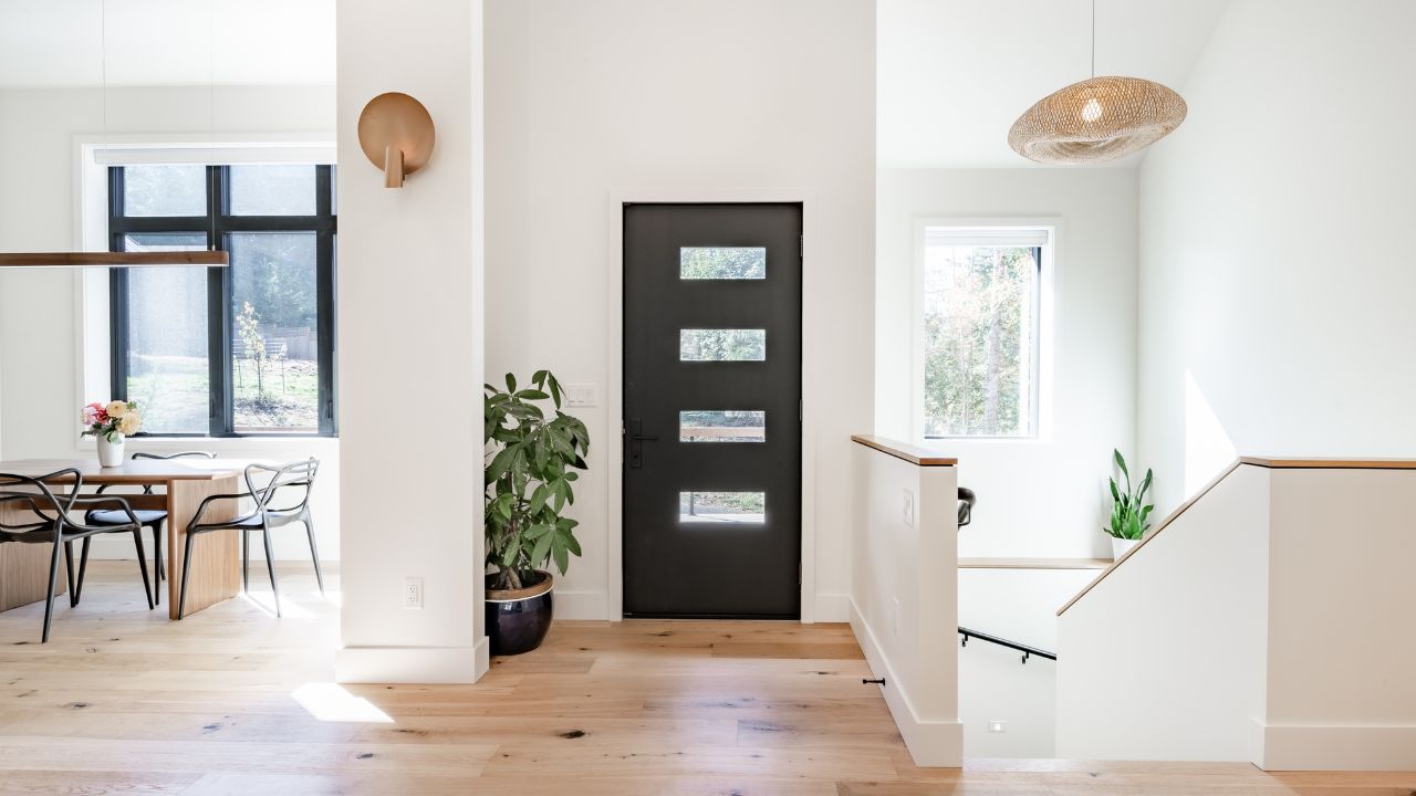 A minimalist entryway with a black front door and plants near the staircase.