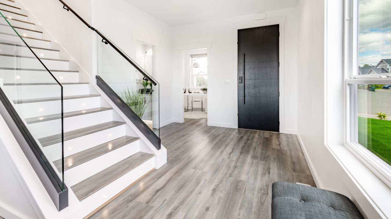 A minimalist entrance hall with a black door, stylish staircase, and a hard word flooring.