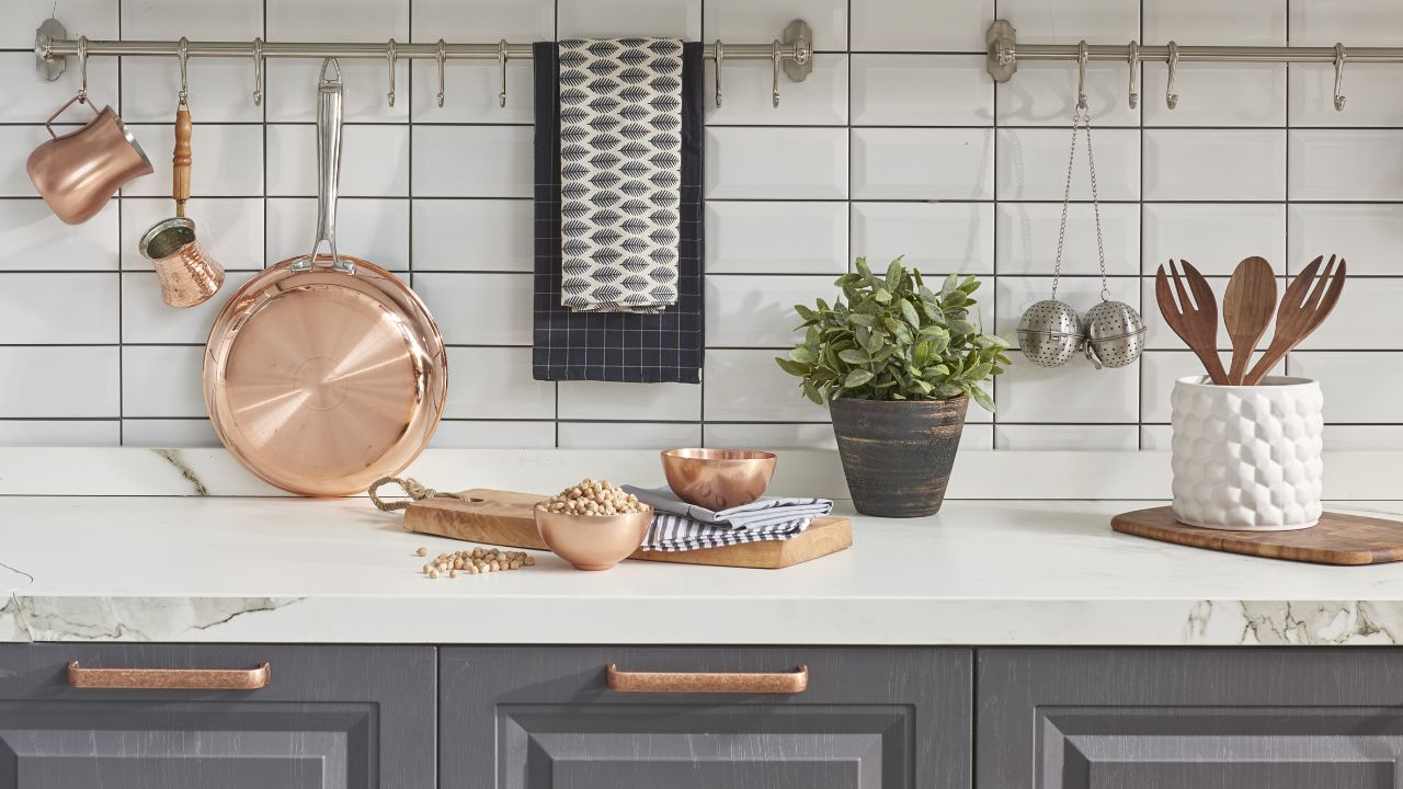 Kitchen with hanging copper pots, cups, and a plant on a white counter.