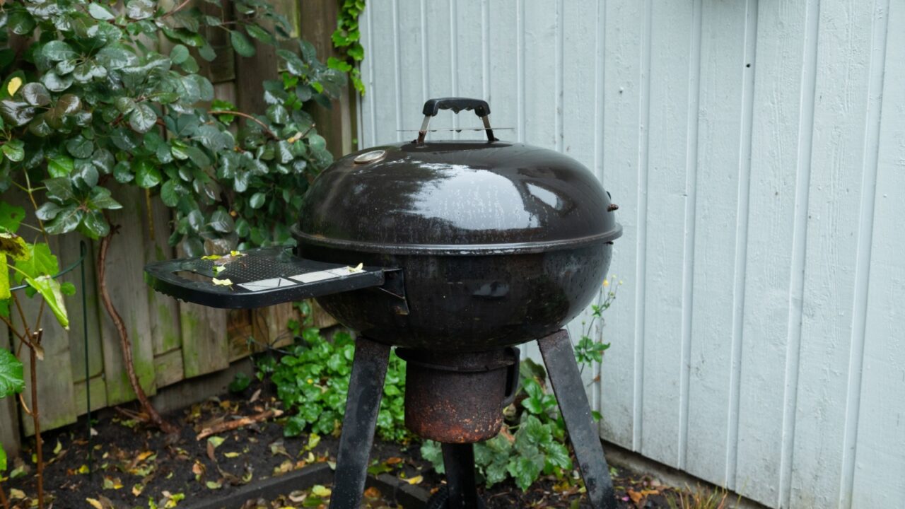 An old kettle grill stands in a backyard, showing signs of weathering