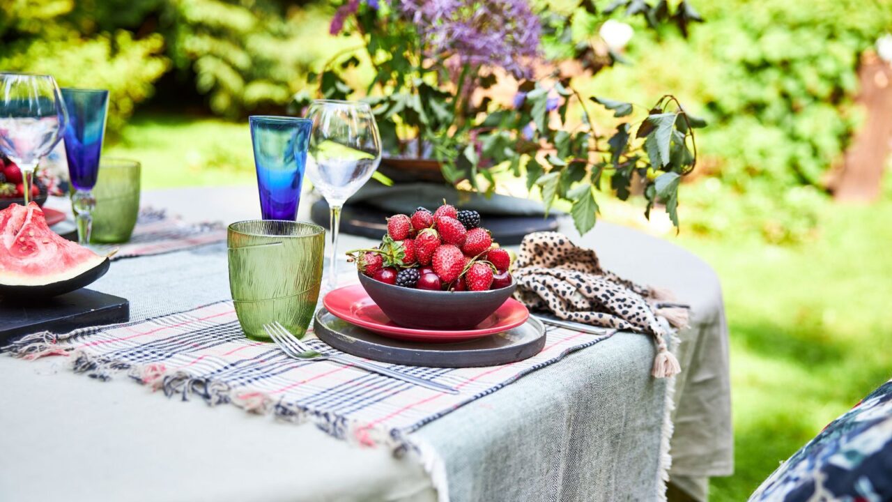 An beautiful outdoor dining setup with plates, cutlery, glassware, and a bowl of berries on a table.