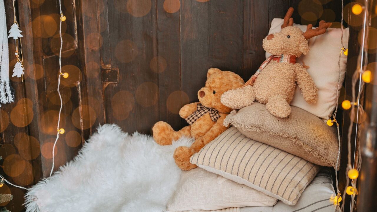 A cozy nook with throw pillows, faux fur throw, stuff toys, and string lights.