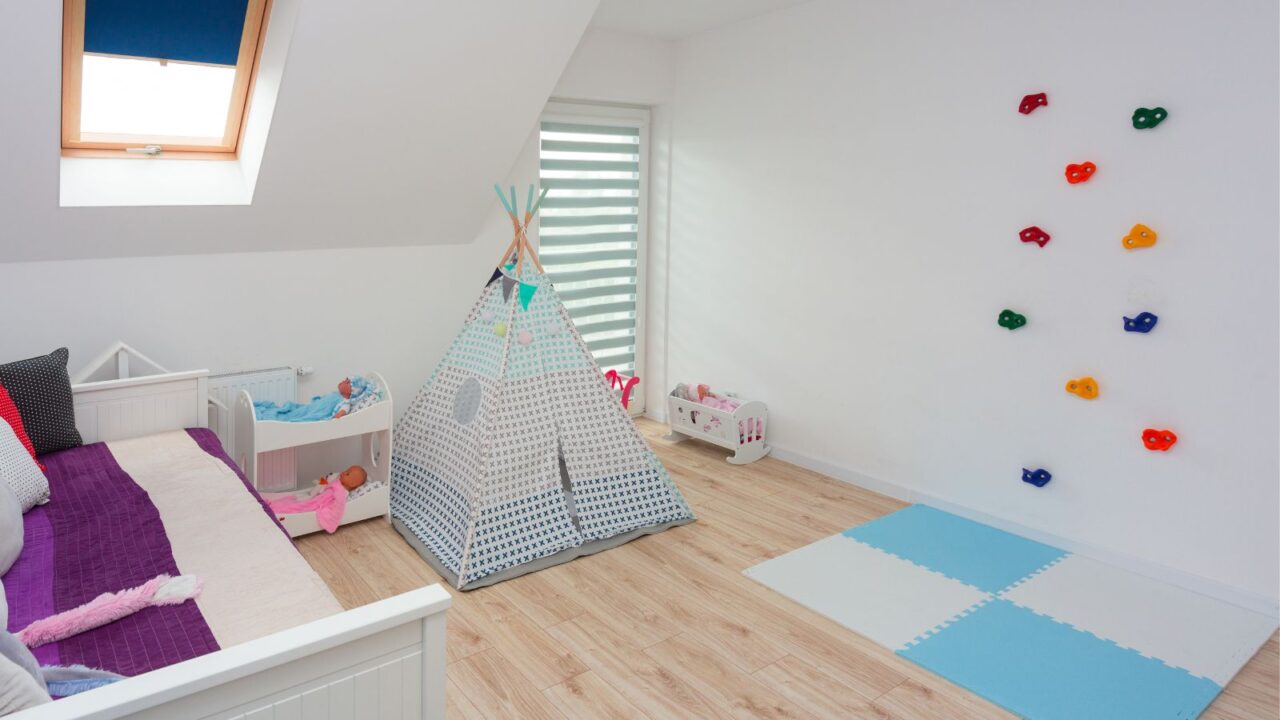 A playroom interior with a cozy sofa, canopy tent, and a colorful climbing wall with soft foam floor mats.