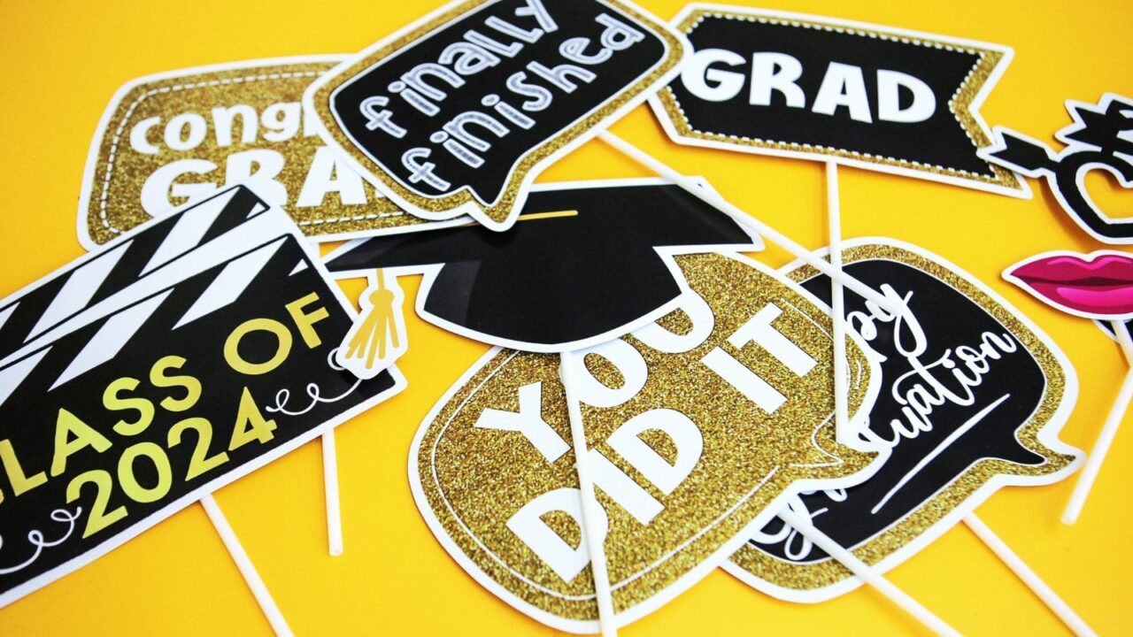 Black and gold graduation party themed props placed on a yellow table.