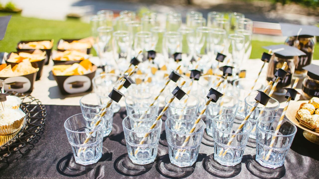 A drink station with clear glasses arranged on a table with yellow and white straw with tiny grad caps.