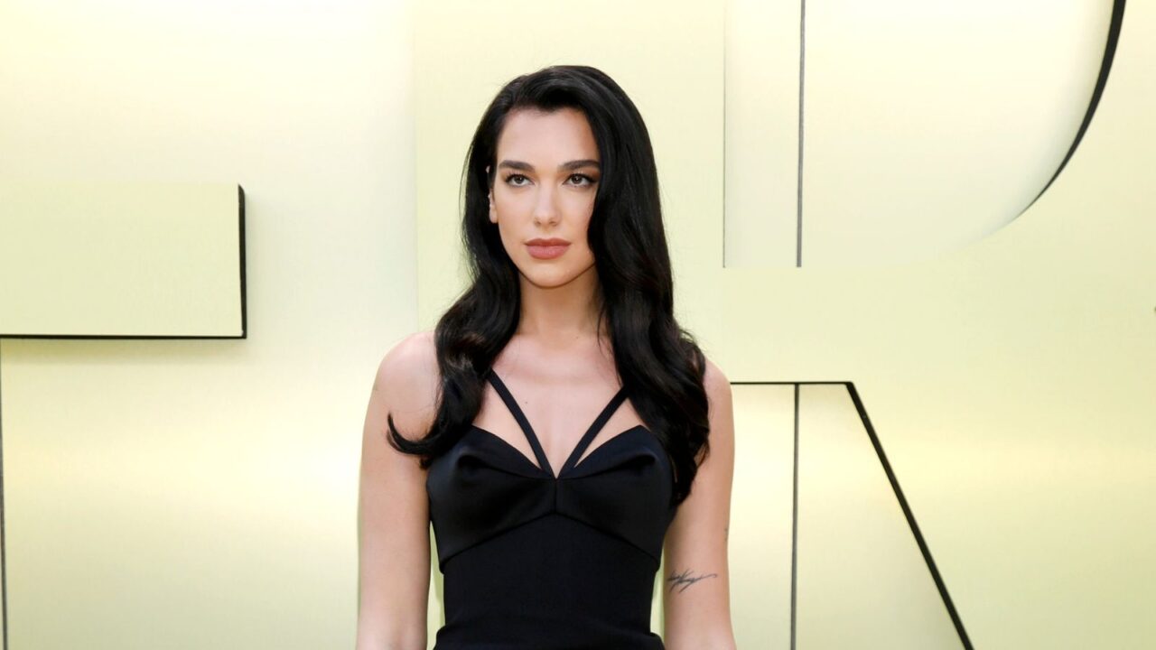 Singer Dua Lipa wearing a beautiful black dress and posing at an event.
