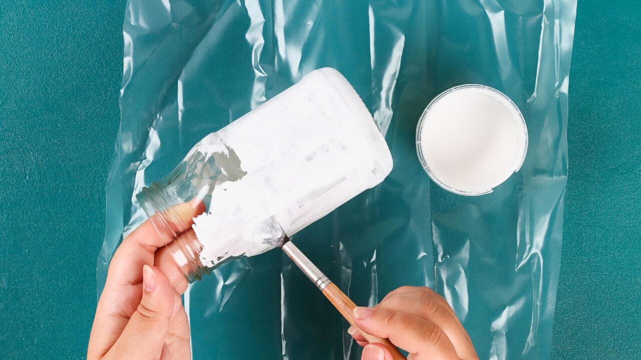 A woman painting a mason jar using white paint.