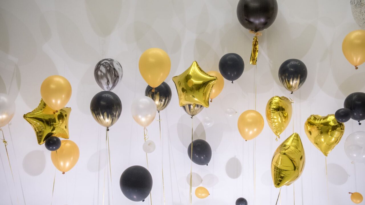 Black, gold, and white balloons tied with ribbons against a white wall.