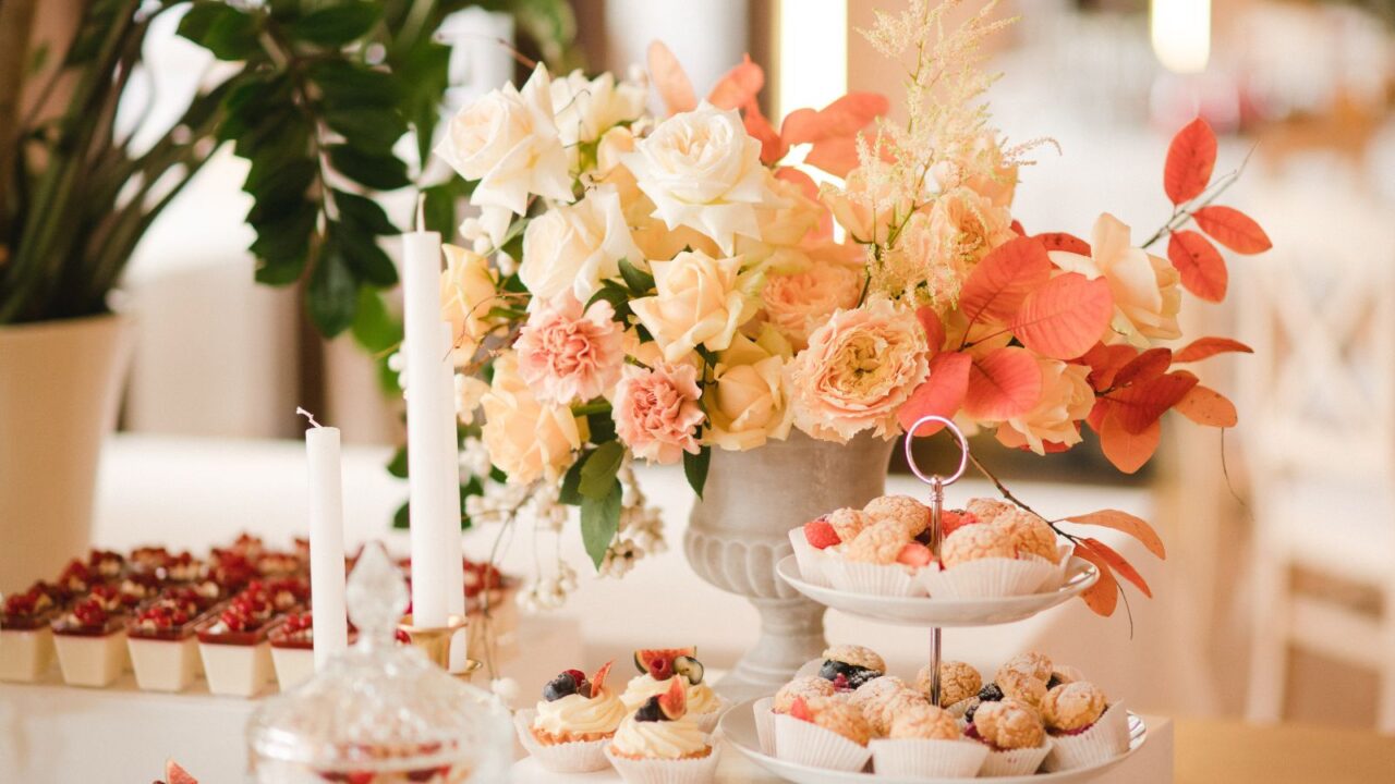 A beautiful dessert table setting with fresh flowers arranged in a vase, candles and sweet treats.