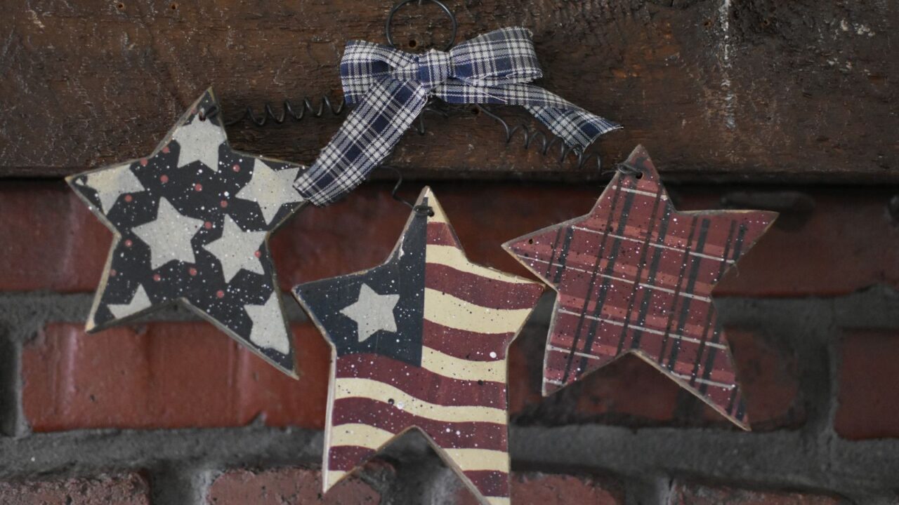Wooden starts hanging on a brick wall with stars, checkered patterns, and USA flag painted on them.